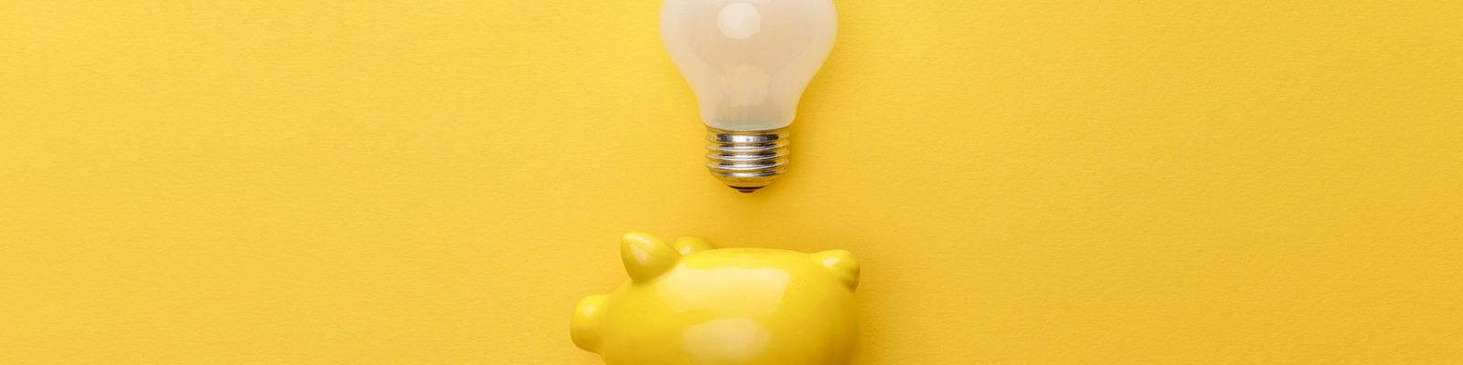 top view of piggy bank with light bulb on yellow background